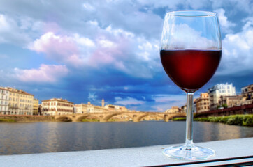 Glass of red wine with view of bridge in Florence during sunset - Ponte alla Carraia,  five-arched bridge over Arno River in the Tuscany region of Italy. Beautiful blue with pink sky.