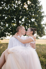 Bride and groom of the background of big tree in the field kiss each other