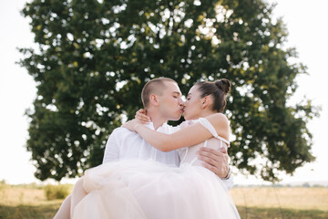 Bride and groom of the background of big tree in the field kiss each other