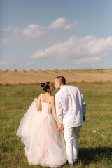 Gorgeous bride with handsome groom walkin in the field after wedding ceremony. Newlyweds posing to photographer