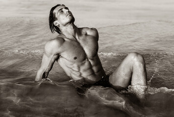 Sexy fit male model with hot strong body lying in the water at the beach. 