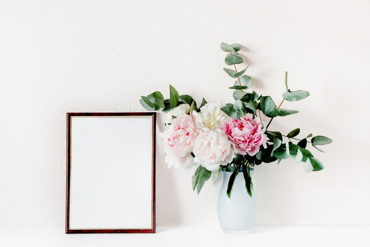Mock up frame with a bouquet of peonies and eucalyptus branches in a vase.