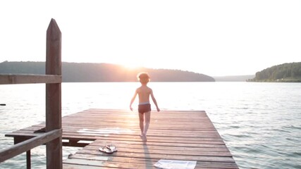 A boy jumps from a pier into the sea or lake in the mountains on warm sunny summer day. - Powered by Adobe