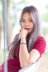 A beautiful Asian woman in a red dress is sitting on a swing in the garden. Portrait asian girl are sitting on wooden chair with looking at camera.