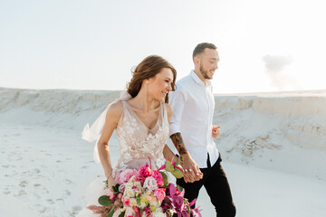 Love Story of a beautiful couple in a pink wedding luxury dress with a bouquet in the Sahara...