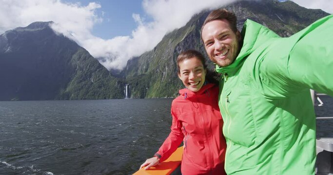 Couple having fun taking selfie video using smart phone on cruise ship, Milford Sound, Fiordland National Park, New Zealand. Multicultural couple smilng having fun laughing on travel vacation.