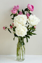 Fototapeta premium Simple sloopy flower bouquet of pink and white peonies flowers in a transparent vase over pastel background
