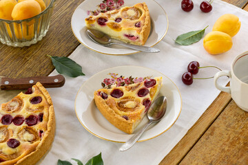 Pieces of summer fruit pie with sour cream filling, apricots and cherries on a wooden table