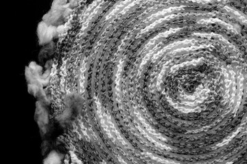 Fragment of a crocheted circle from melange threads based on a plastic canvas from the wrong side close-up. Black and white