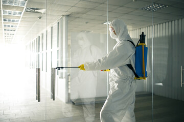 Sanitary worker sprays an empty business center with antiseptical liquid to prevent covid-19...