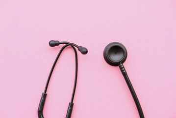 Black modern stethoscope on pastel pink background.