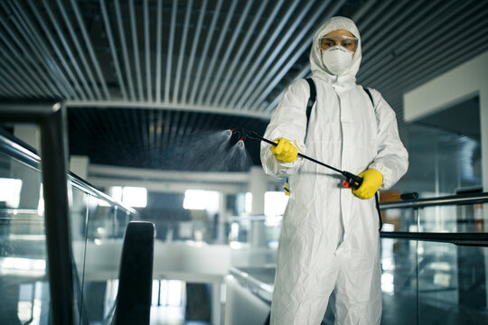 Disinfection worker wearing a protective suit professionally cleans up an escalator in an empty business center. A man equiped with antibacterial clothes sterilizes shopping mall. Covid concept.