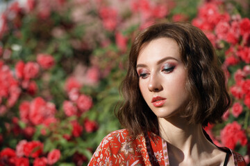 Naklejka premium Young beautiful dreamy woman with red roses. Outdoor portrait of a romantic girl with hard sunlight. Space for text.