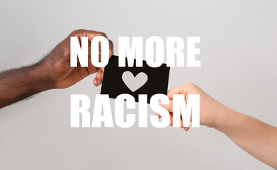 Hands of Caucasian woman and African-American man holding paper sheet with drawn heart on grey background. Concept of racism