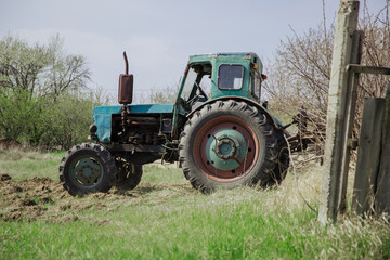 An old blue tractor plows a field and cultivates the soil. Agriculture.