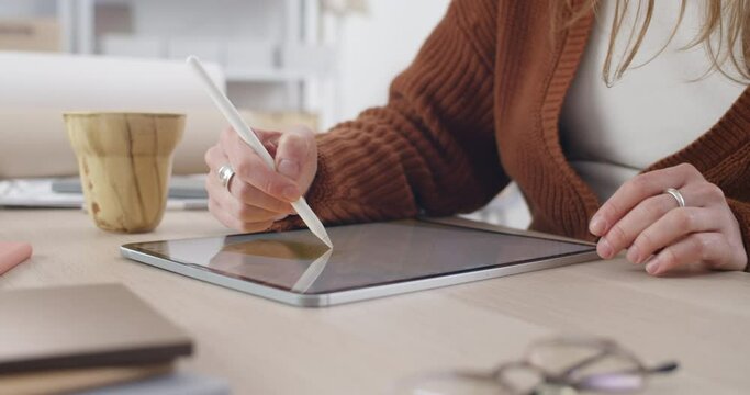 Crop view of female web designer creating picture while drawing on digital pad and touching screen. Female person using tablet and stylus while sitting at table. Zoom in