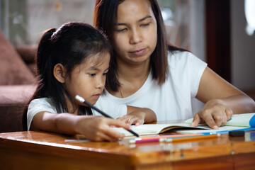Young asian mother helping her daughter do her homework at home. Education from home concept.