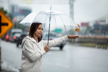 Asian woman holding umbrella hitchhiking taxi at city street in the rainy day.