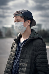 teenage boy poses in a city street, wearing a protective face mask - the concept of modern life and virus protection