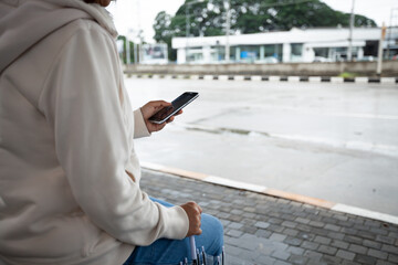 Asian woman is using on smartphone, checking social media network  while waiting taxi at bus stop in the rainy day.