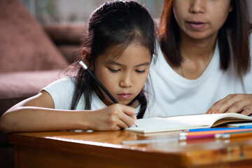 Young asian mother helping her daughter do her homework at home. Education from home concept.