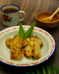 Indonesian traditional food of fried banana with pandan leaves served in a metal plate with palm sugar powder and a cup of hot tea