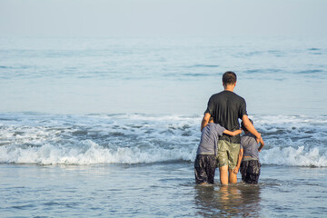 father day. father and his two sons playing in the beach, father gives protection to his sons