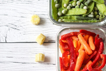 Frozen vegetables such as green peas, pea pods, green beans, red sweet pepper and baby carrot in the transparent bowls on the concrete wooden background with copy space, top view