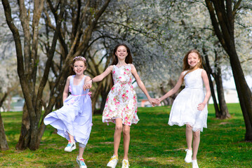 Naklejka na ściany i meble Three beautiful girls in retro dresses for a walk in a flowered garden. The idea and concept of a friendly family and a happy childhood.