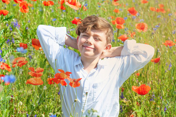 Happy boy in a white shirt on a meadow of blooming red poppies. Enjoyment. Harmony with nature. Boy...