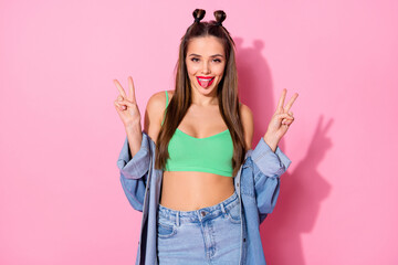 Photo of pretty nice funky lady showing v-sign symbol sticking tongue out mouth wear denim jacket green crop top modern clothes isolated pastel pink color background