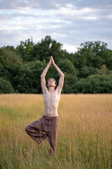 Shirtless man practicing tree pose while standing on landscape in forest