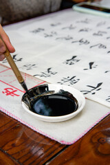 A calligrapher is creating calligraphy, dipping a brush into ink