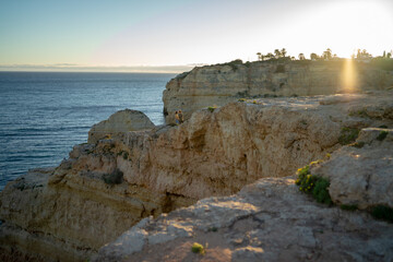 Distant view of couple standing on cliff by sea against clear sky at sunset