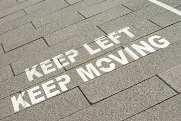 Angled view of white lettering on pavement, advising pedestrians to keep to the left hand side and to keep moving. UK government warning sign during the Coronavirus pandemic crisis.