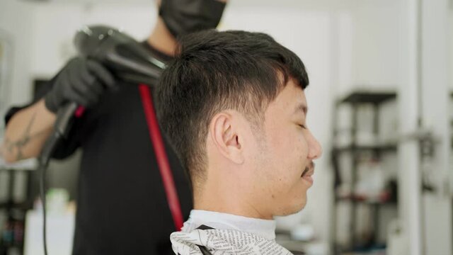 side view Asian man get hair blow dry. During pandemic period, electric hair blow dryer, at guy barber, new normal, social distancing, Corona virus Covid-19 re-open business star up local home shop