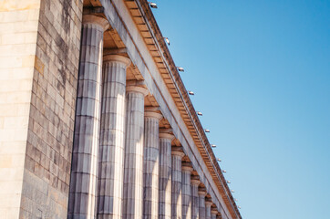 A side angle view of a big aged architectural building with columns and a clean sky in the afternoon.