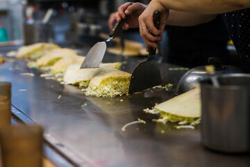 Hand making a Japanese Hiroshima style layered pancake, Okonomiyaki, on a hot pan.