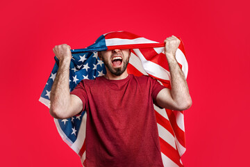 Caucasian man with an American flag on his head throws his hands up and shouts. Red background. The...