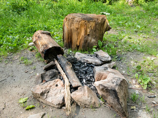 Fototapeta premium Stone camp fire pit with a log or stub for sitting down . Burnt wood in a camp fire