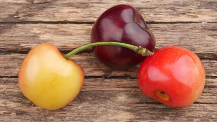 Three ripe cherries of different colors close-up on an old wooden table.
