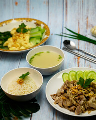 hainan chicken rice complete with chicken broth, tofu, sliced cucumber and pak coy on blue vintage table