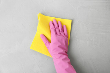 Woman in gloves wiping grey table with rag, top view
