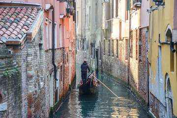 Fototapeta na wymiar a gondola driven by a gondolier sails along a narrow channel between houses in Venice