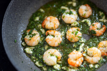 Shrimps with herbs and garlic oil are fried in a pan, cooking seafood concept, selected focus
