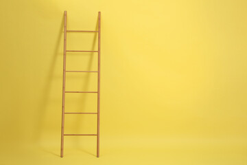 Modern wooden ladder on yellow background. Space for text