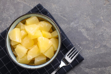 Tasty canned pineapple in bowl on grey table, flat lay. Space for text