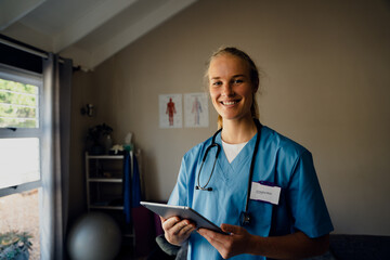 Portrait of young beautiful Caucasian female doctor in scrubs with digital tablet, smiling