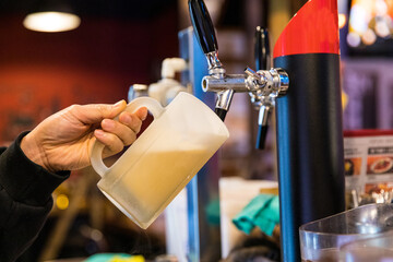 Hand pouring a fresh frozen glass of beer from a beer tap dispenser.