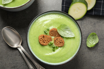 Tasty homemade zucchini cream soup served on grey table, flat lay